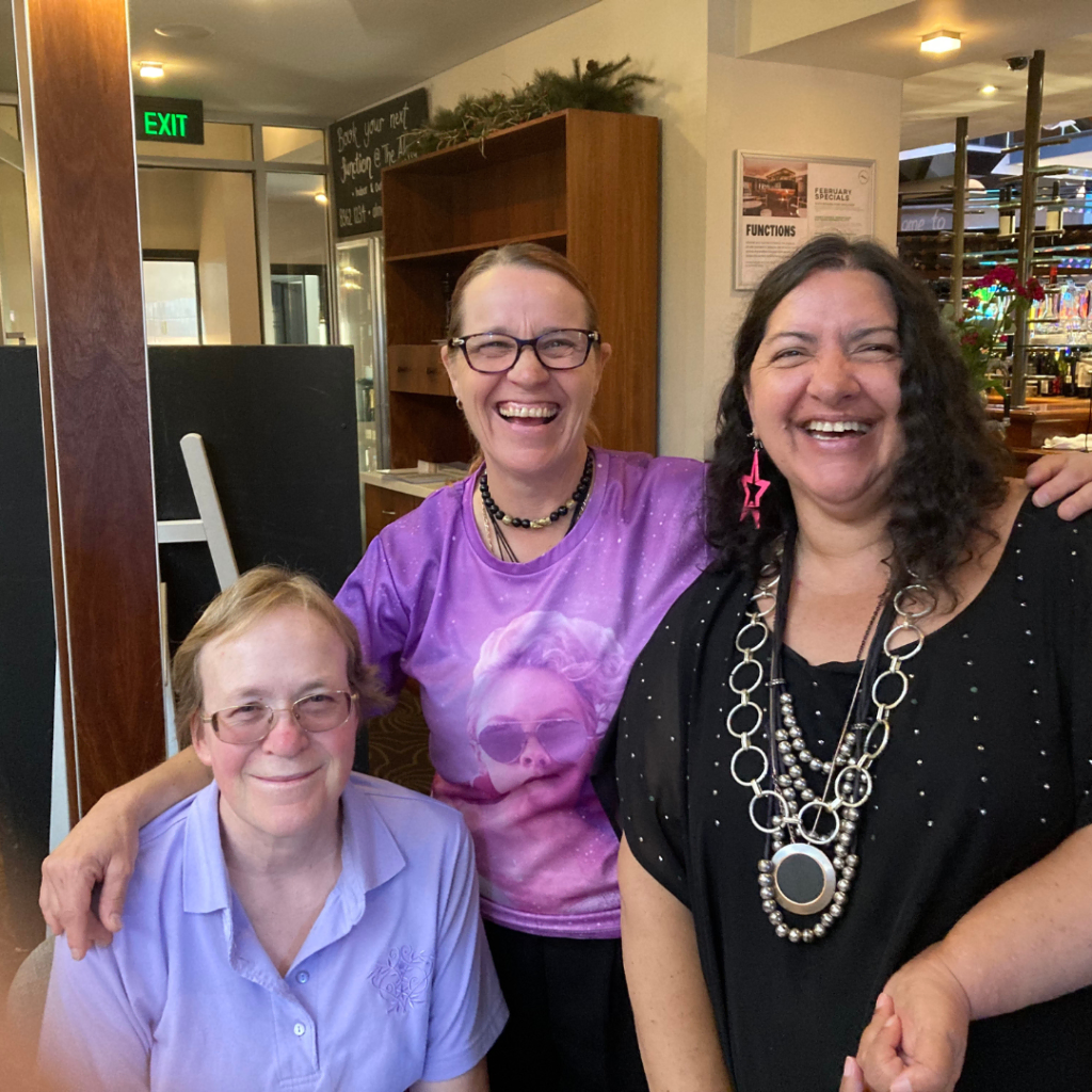 Three women smiling for the camera in a restaurant.