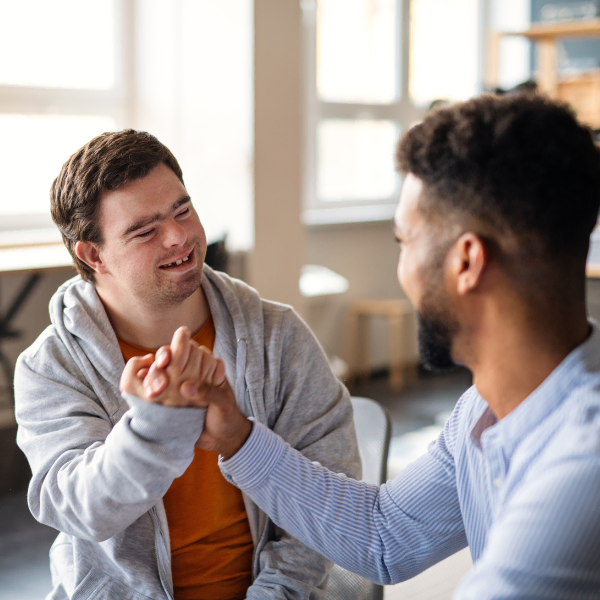 A teenage male NDIS participant sitting at a kitchen table, high fiving his Disability Support Worker