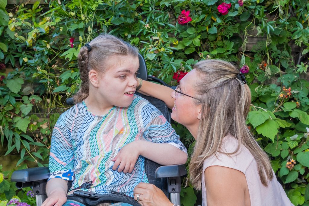 A young female NDIS participant in a wheelchair, in a garden, being supported by a female Enhanced Lifestyles Disability Support Worker.