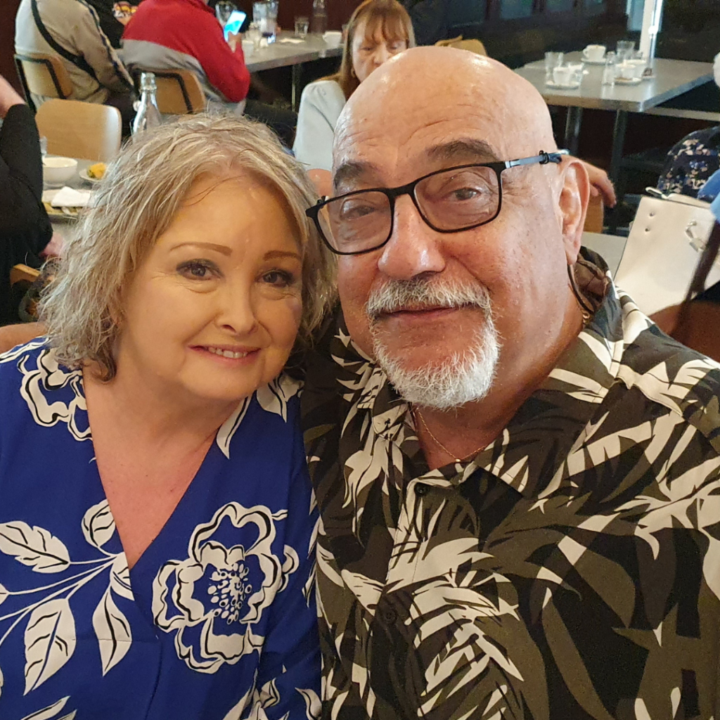 Two smiling adults posing for a close-up selfie in a restaurant setting.