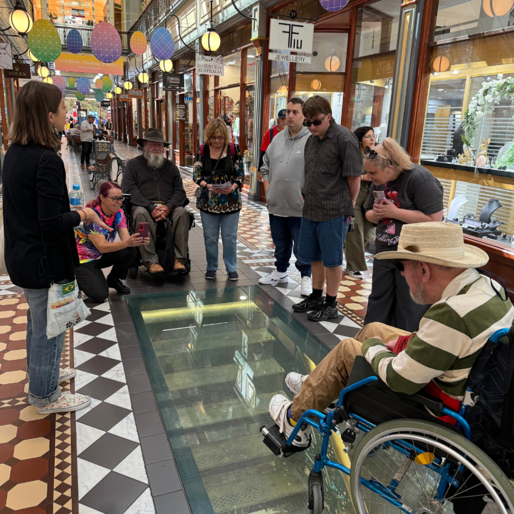 People gathered around a glass floor exhibit inside a shopping arcade.