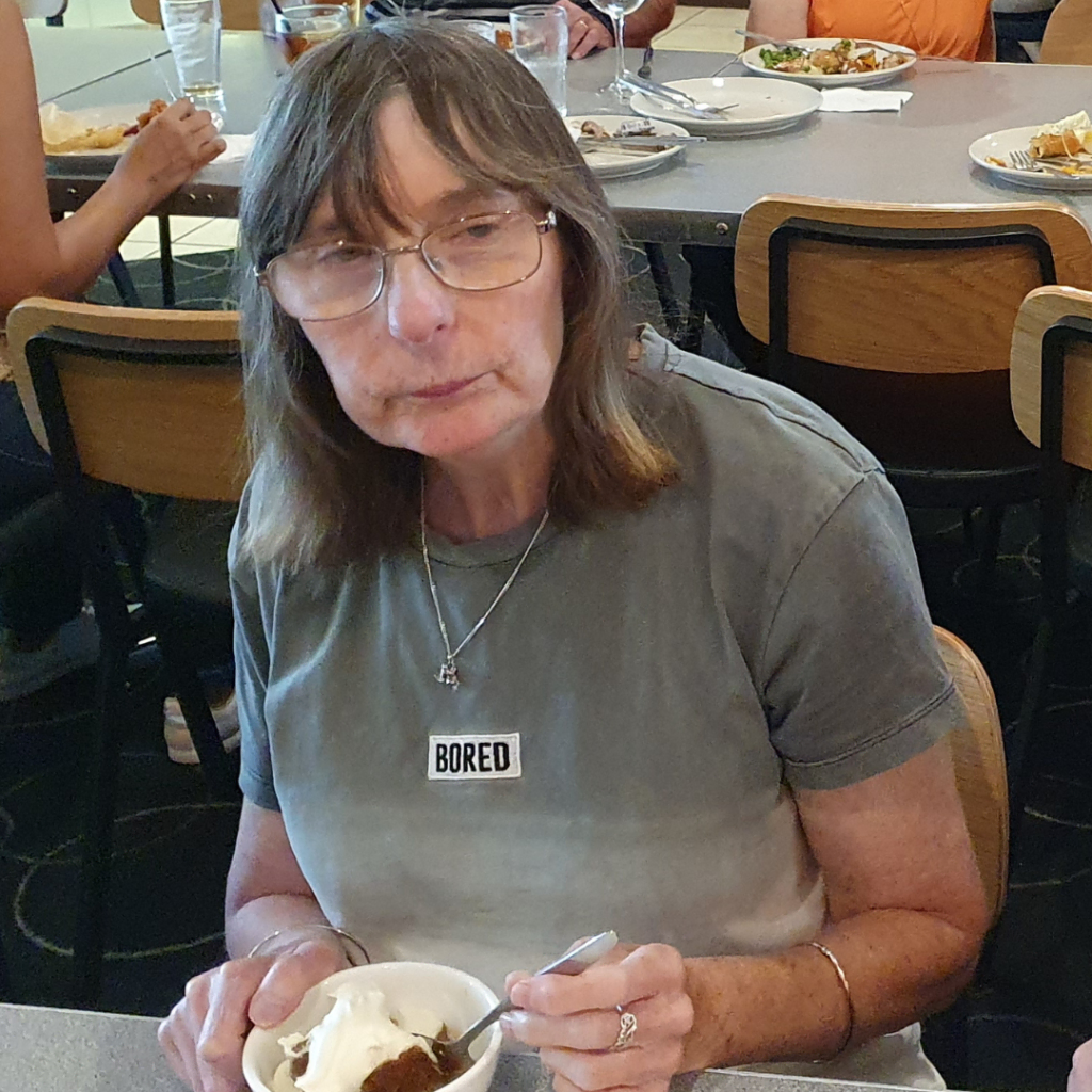 Woman wearing a "bored" necklace eating ice cream at a table.