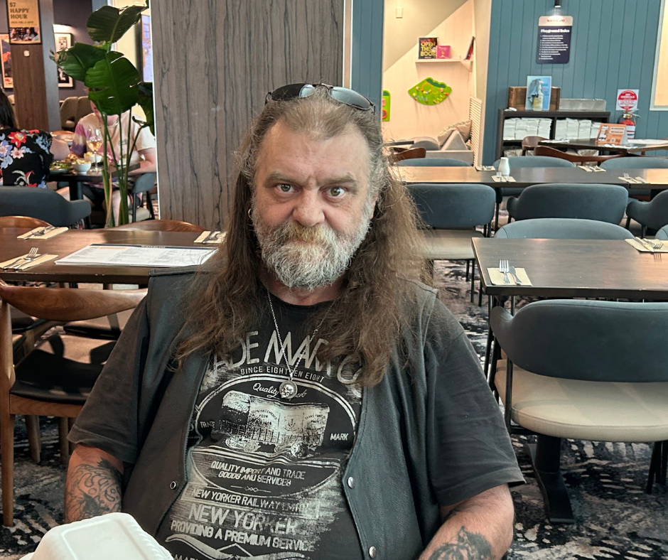 A man with long hair sitting at a table in a restaurant.