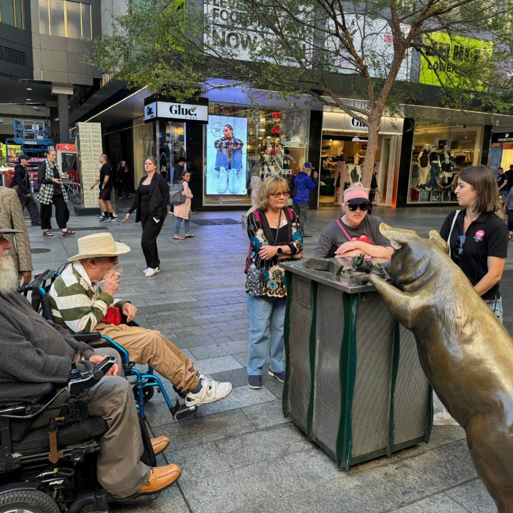 People interacting with a bronze pig sculpture in a pedestrian mall.
