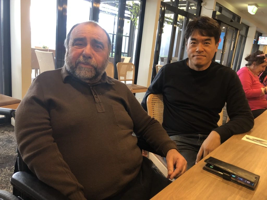 Two men in wheelchairs sitting at a table.