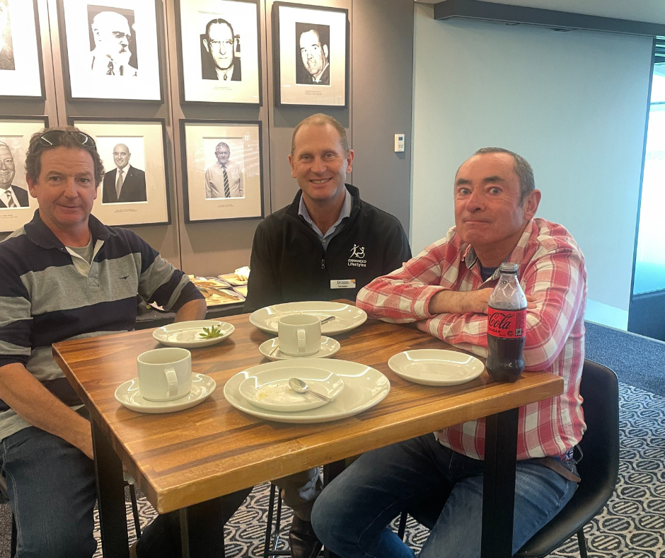 Three men sitting at a table with plates and cups.