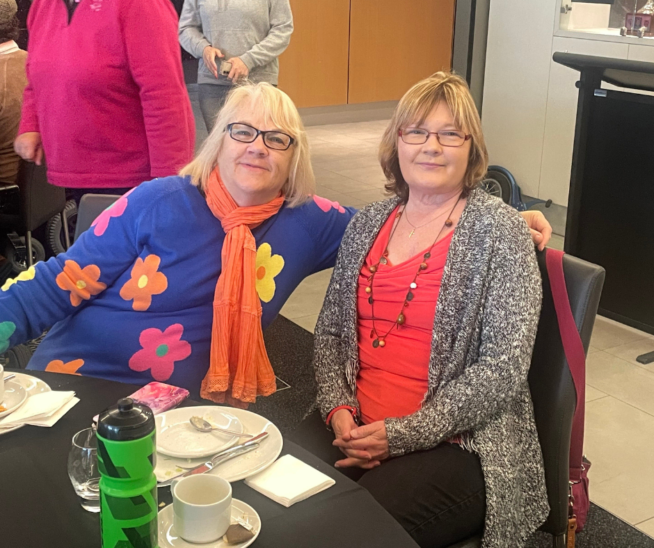 Two women posing for a picture at a table.