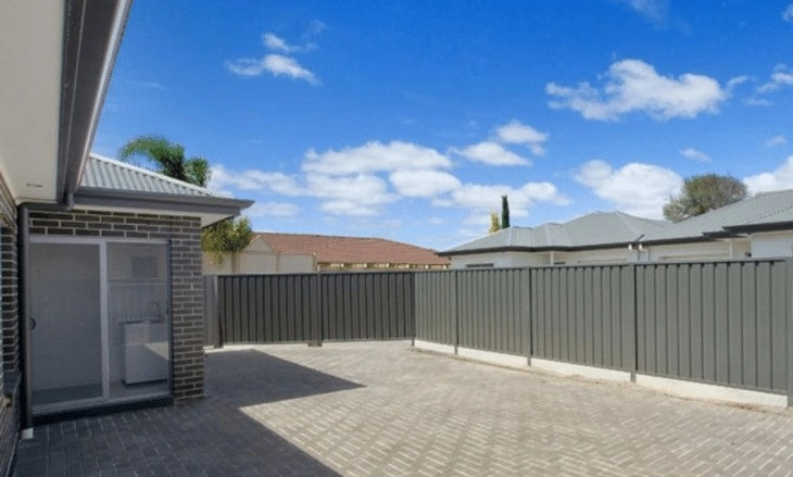 A paved backyard, with grey fencing around the outside. The house has a sliding door leading directly into the laundry which has a sink.
