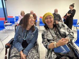 Two women in wheelchairs smiling while sitting in a room.