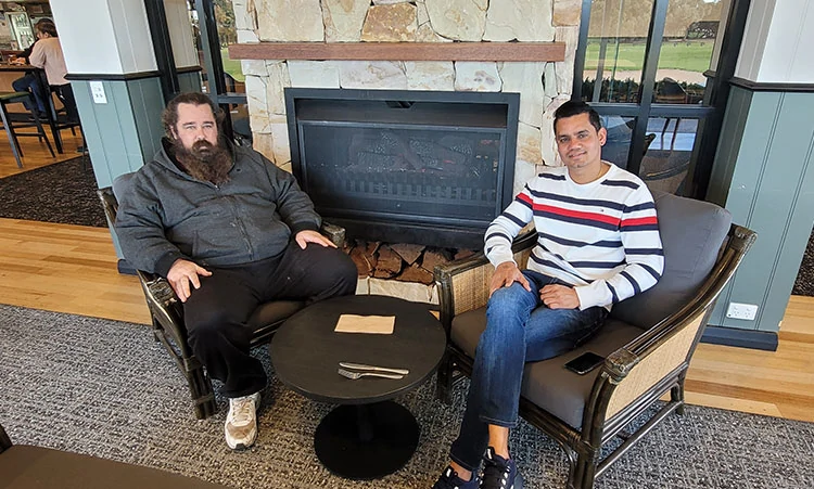 Two men in casual clothes seated in front of an open fire