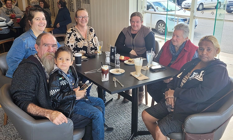 Seven people of different ages and gender are seated around a table with their milkshakes and coffee in front of them.