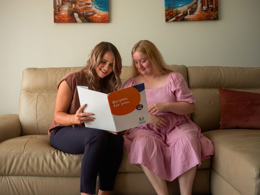 Two women sitting on a couch looking at a brochure.