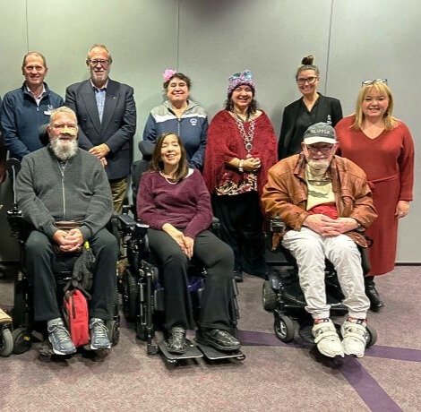 Group of adults posing for a photo, some standing and some in wheelchairs.