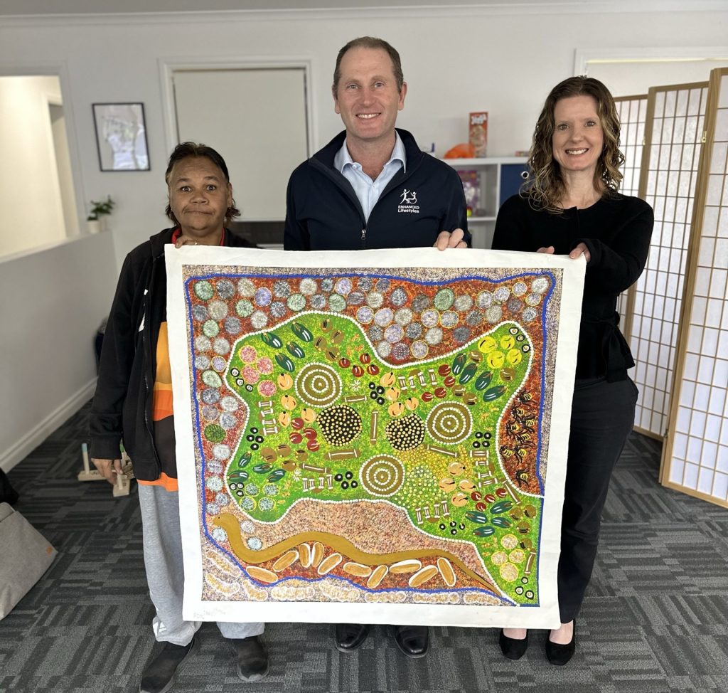 Three people holding a large painting in an office.