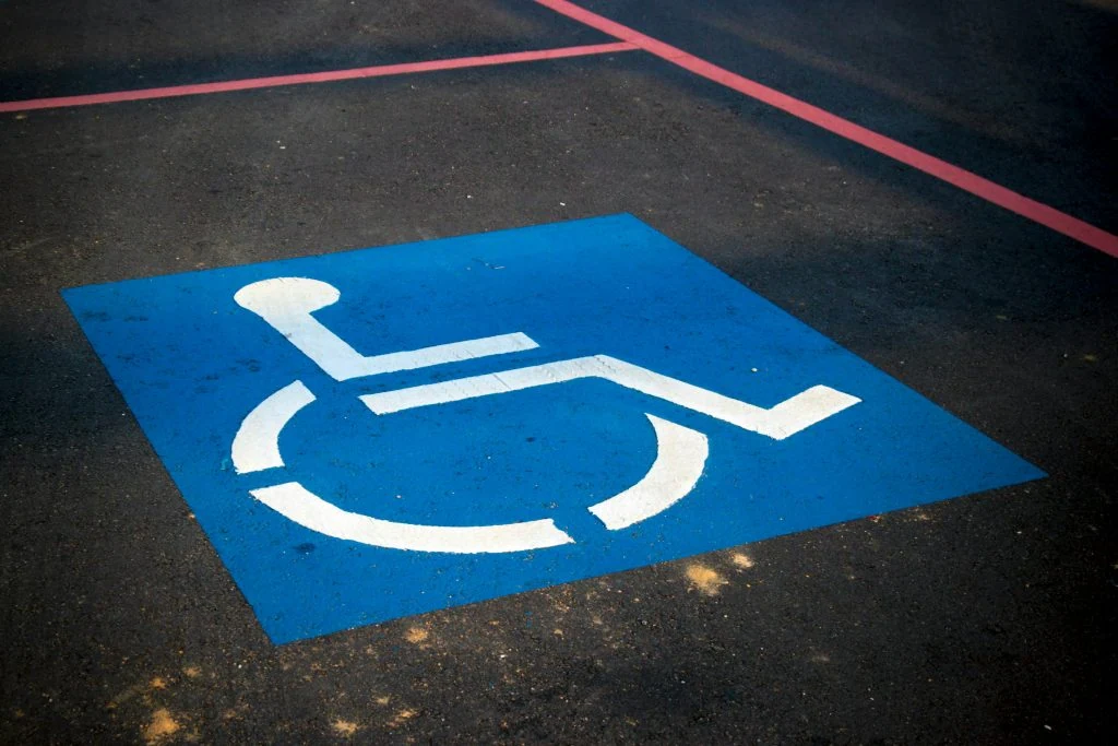 A blue and white disabled parking symbol painted on an asphalt surface, bordered by pink lines.