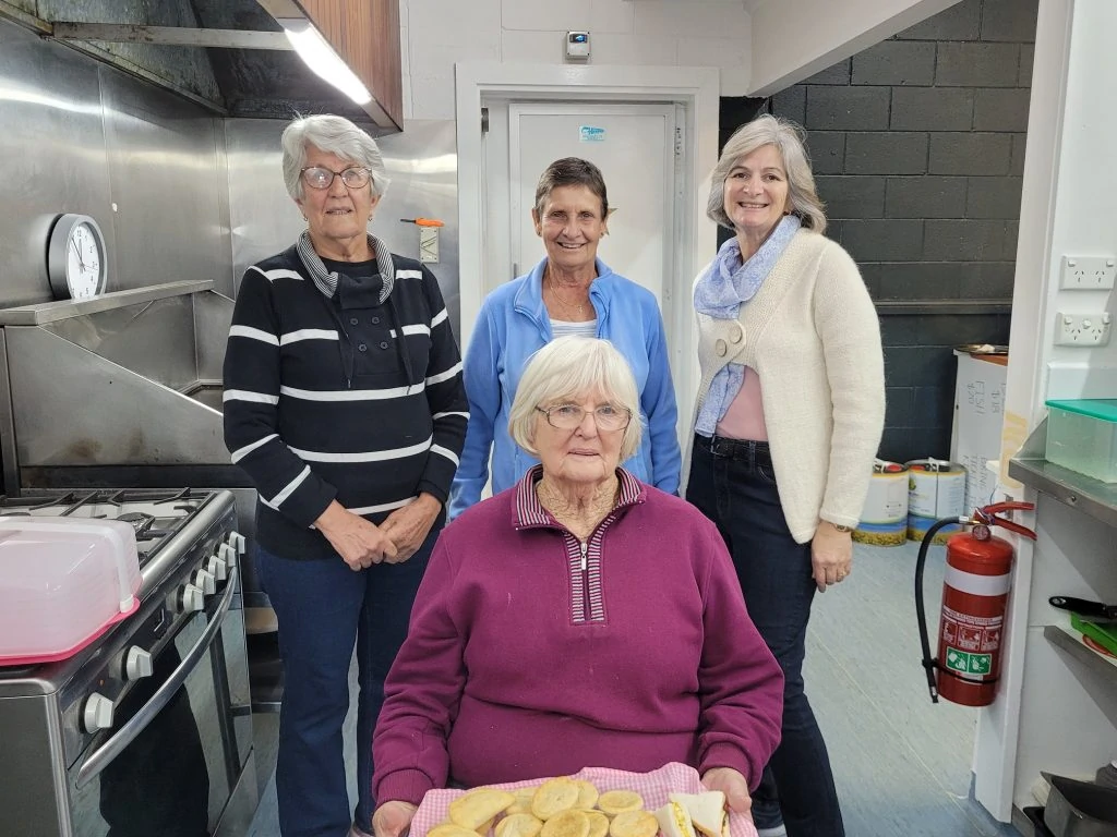 Four ladies standing in the kitchen showing the delicious sandwiches they’ve made. 