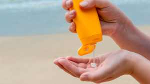 A person's hand holding a bottle of sunscreen on the beach.