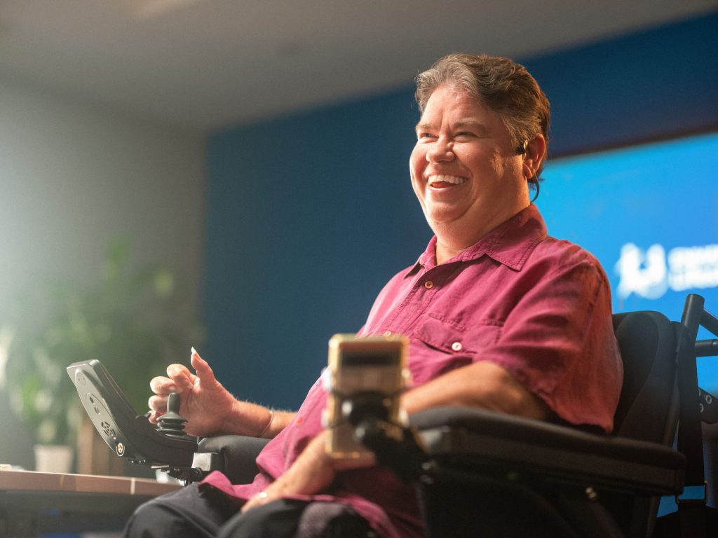 A man in a wheelchair smiling in front of a screen.