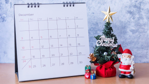 A calendar with a santa claus figurine next to it.