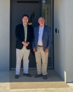 Ken and William Fryer standing in front of a modern SDA house.