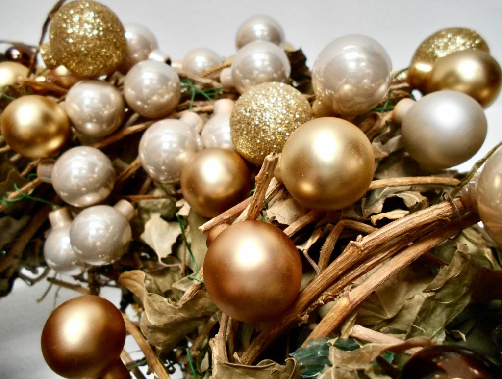 Golden and pearl-colored ornaments clustered with dried leaves and twigs.