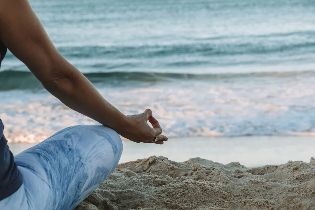 Person meditating on a sandy beach with ocean waves in the background.