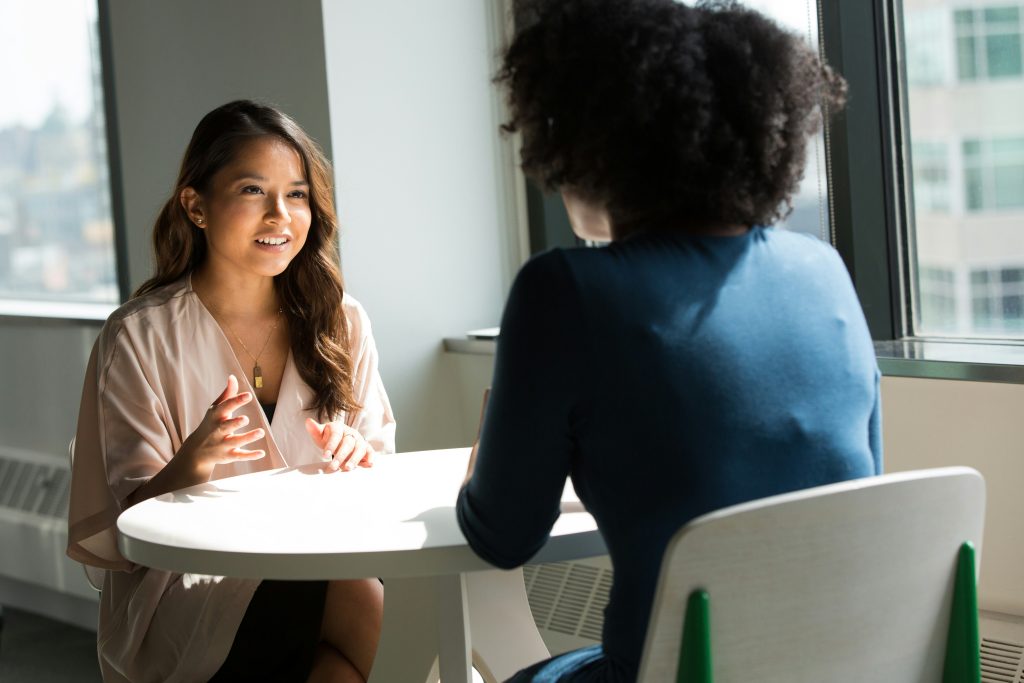 Two people sitting at a round table in a bright office setting, engaged in conversation.