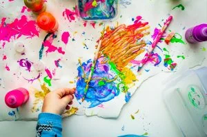 A child is painting with colorful paints on a white table.