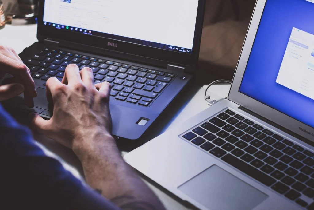 A person types on a Dell laptop while another open laptop sits beside it.