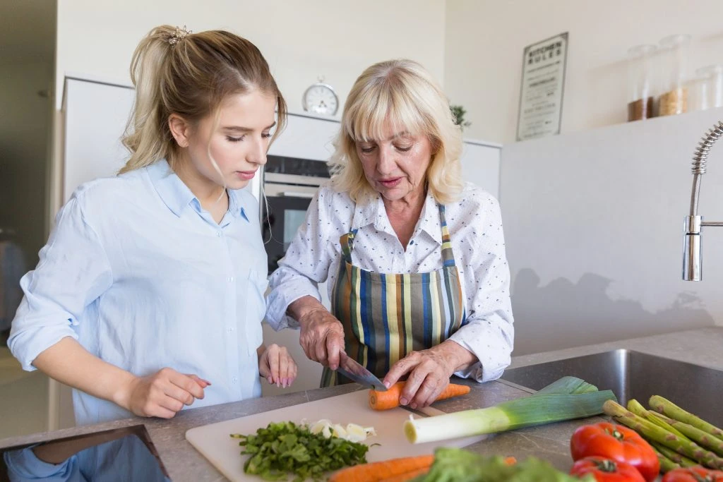 Grandmother teaching her granddaughter how to make a salad at the kitchen