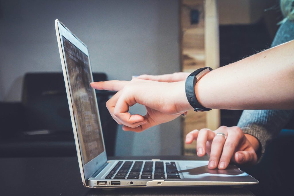 Two hands are shown interacting with a laptop; one hand points towards the screen while the other rests on the keyboard.