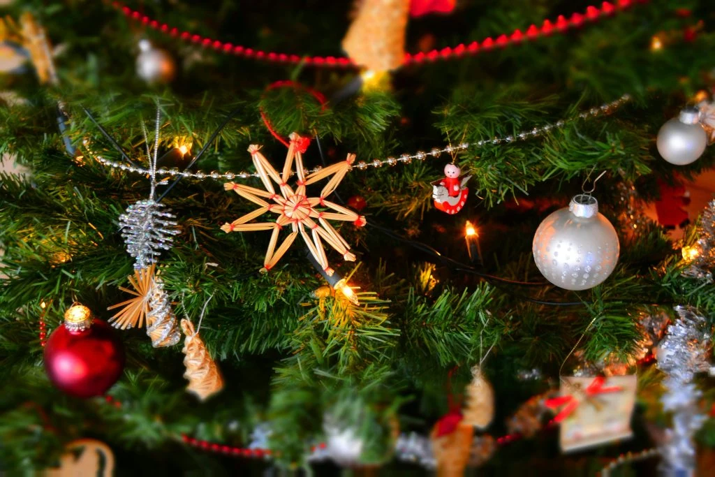 Close-up of a Christmas tree decorated with a straw star ornament, red and white Santa figure, silver and red baubles, and pine cone ornaments.