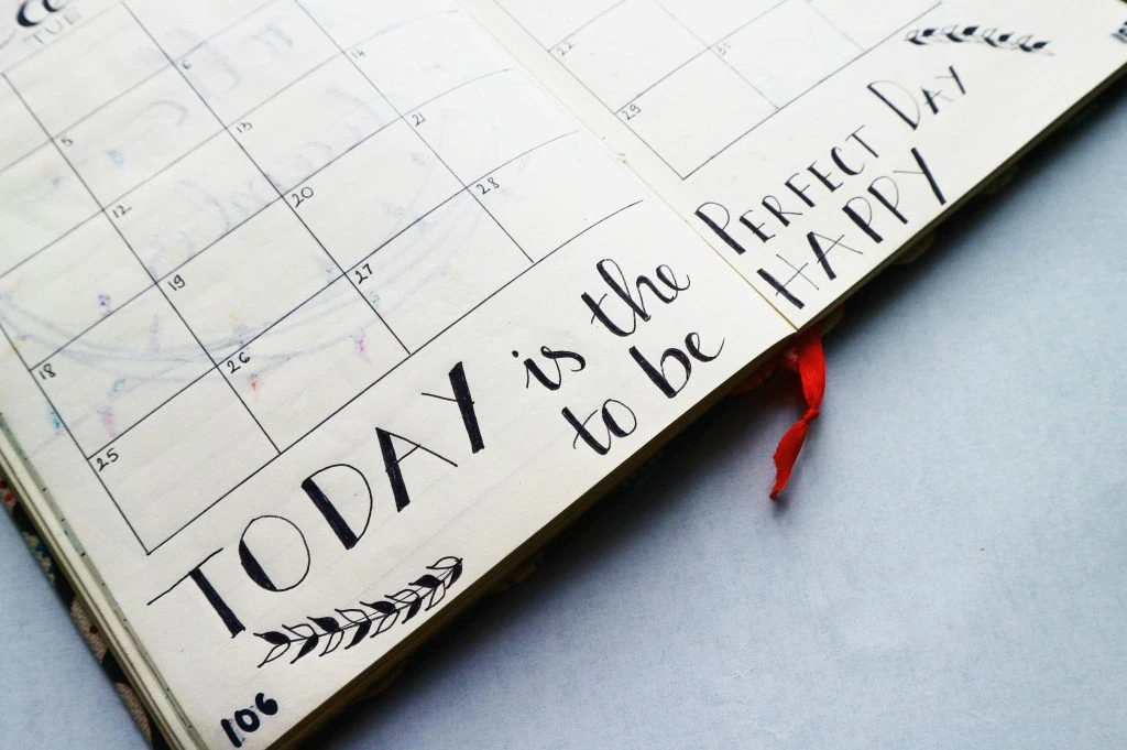 Open planner with a handwritten message: "Today is the perfect day to be happy" on a blank calendar page.