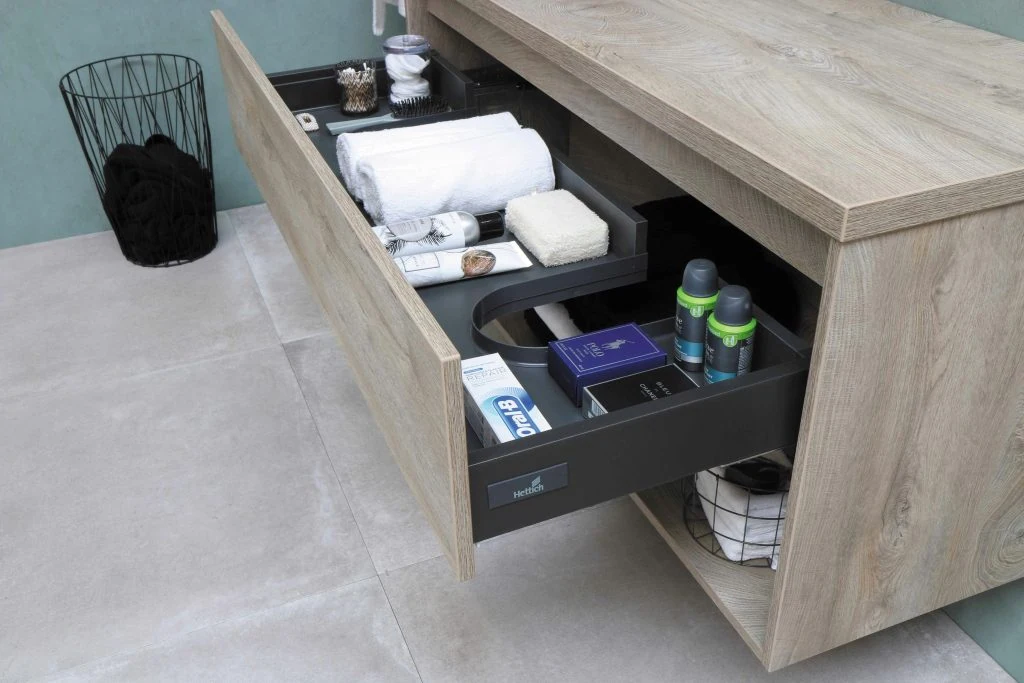 A modern bathroom vanity drawer open, revealing organized toiletries, towels, and bath products.