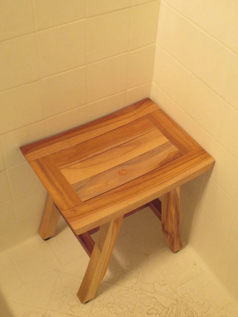 A small wooden stool in the corner of a tiled shower.