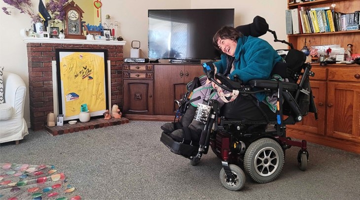 A female NDIS participant sitting in her lounge smiling