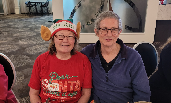 Two women sitting at a table with santa claus hats on.