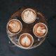 Four cups of latte with intricate latte art patterns are arranged on a wooden surface.