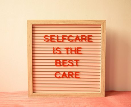 A framed letter board with the message "Selfcare is the best care" in red letters against a peach background.