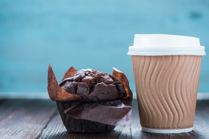 A cup of coffee and a chocolate muffin on a wooden table.