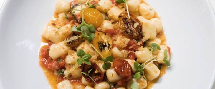 A bowl, with gnocchi, in a sauce of red and yellow cherry tomatoes garnished with cress and fried breadcrumbs
