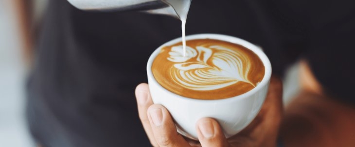 A man holding a coffee cup in his hand, creating milk art