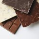 Assorted chocolate bars stacked: dark, milk, and white with nuts, on a white background.