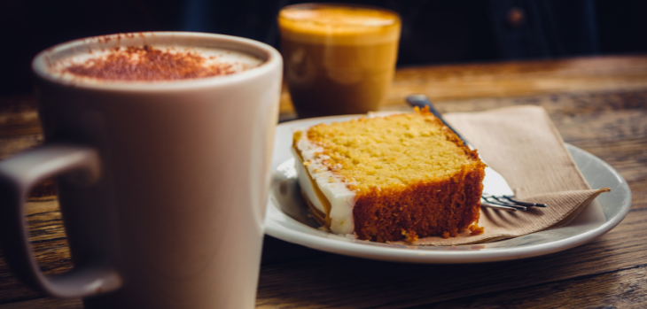 A piece of cake on a plate next to a cup of coffee.