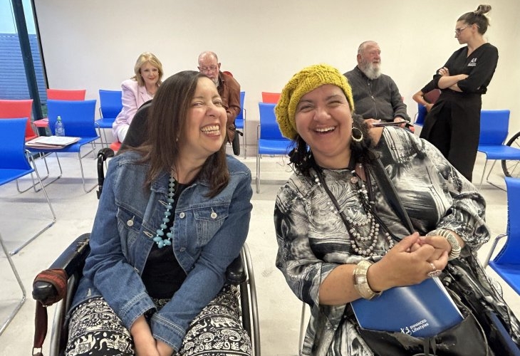 Two women in wheelchairs smiling while sitting in a room.