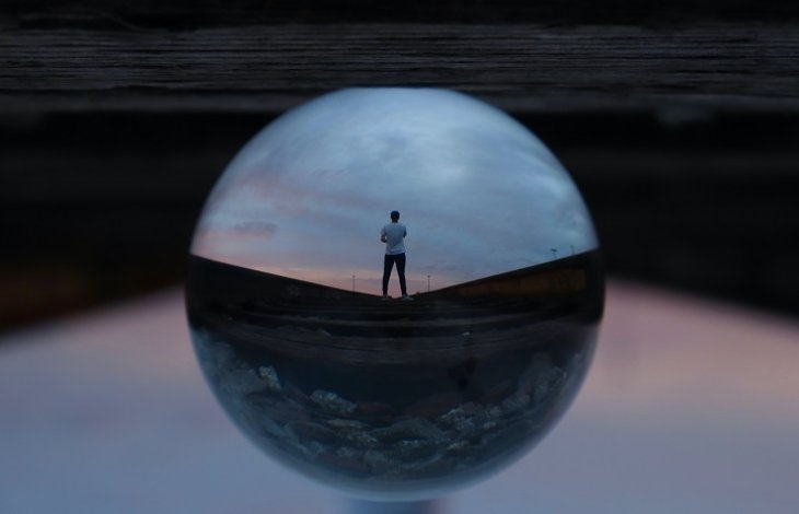 Reflection of a person standing on a railway track, captured through a glass ball.