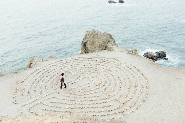 Person walking in a circular rock labyrinth on a cliffside overlooking the ocean.