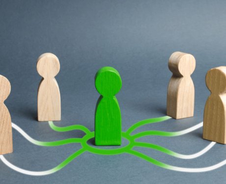 1 green wooden people shapes figure, standing in the middle of 7 brown wooden figures connected to them by lines