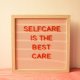 A framed letter board with the message "Selfcare is the best care" in red letters against a peach background.