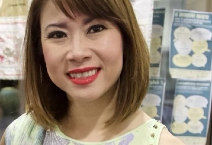 A woman wearing red lipstick and a light green top is smiling.